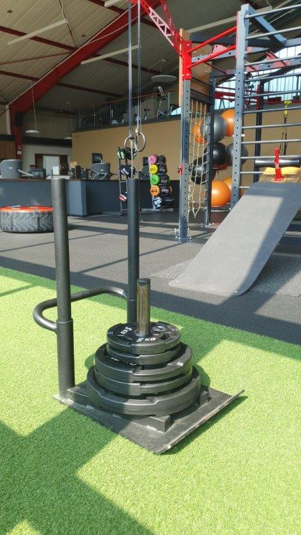 Fitnessstudio mit grünem Boden, Gewichtsschlitten, Klettergerüst, Hantelscheiben und Tragegriffen.