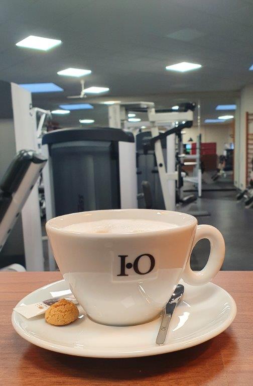 Eine Tasse Kaffee mit einem Keks im Vordergrund eines Fitnessstudios.