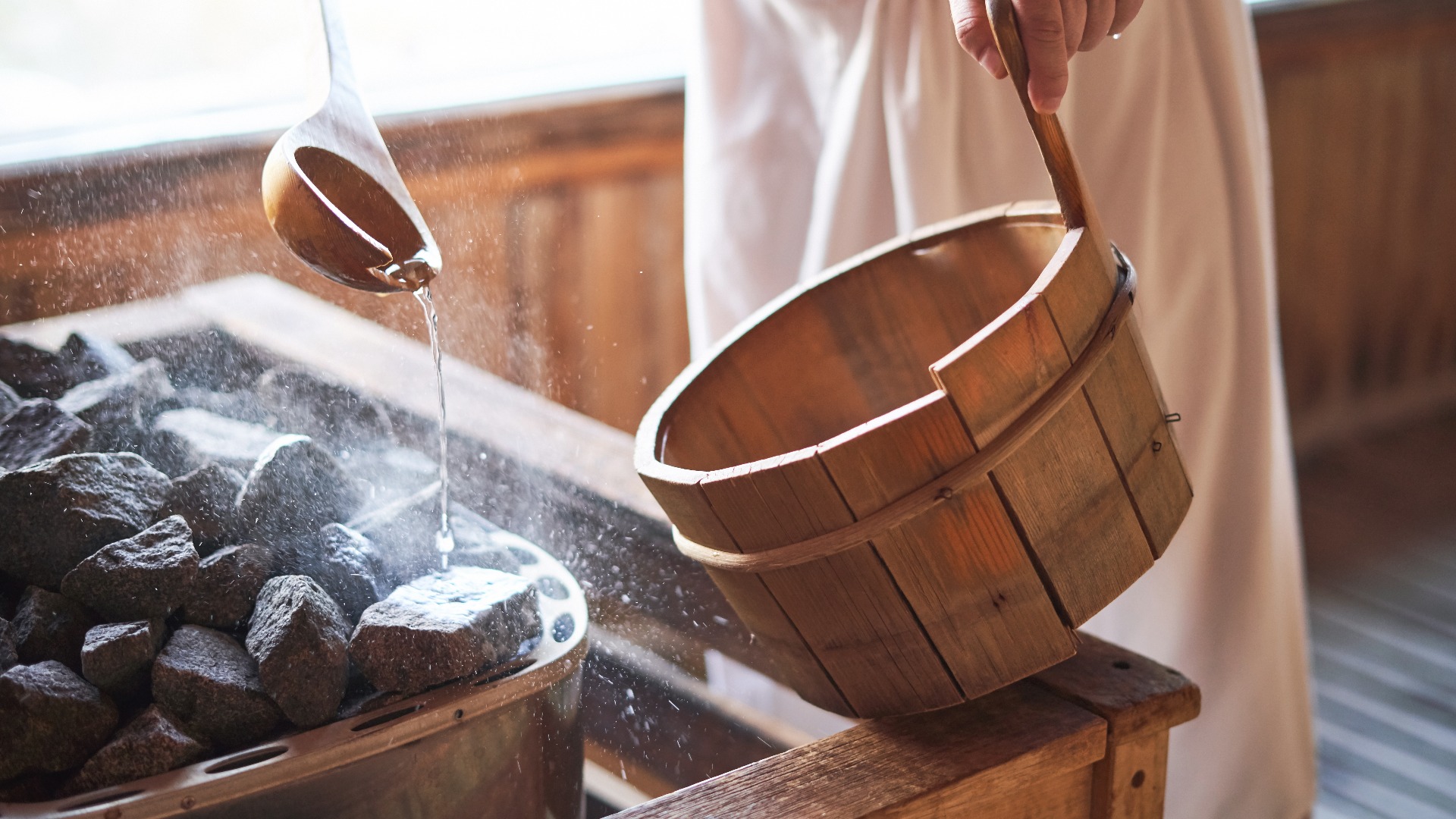 Man pouring water into hot stone in sauna room.